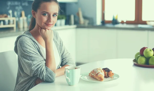 Mujer bebiendo té con croissant dulce en la mesa de la cocina —  Fotos de Stock