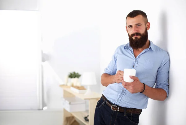 Giovane uomo in piedi vicino alla parete e in possesso di una tazza di caffè — Foto Stock