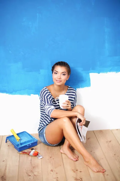 Portret malarza kobieta siedzi na podłodze w pobliżu ściany po malowaniu — Zdjęcie stockowe