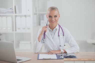 Güzel, genç, gülümseyen bayan doktor masada oturuyor ve yazıyor..