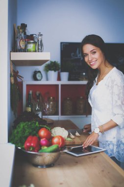 Mutfakta yemek yapmak için tablet bilgisayar kullanan genç bir kadın.