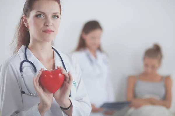 Young woman doctor holding a red heart, standing — Stock Photo, Image