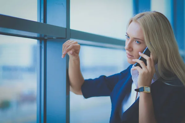 Zakenvrouw staat tegen kantoorraam te praten op mobiele telefoon — Stockfoto