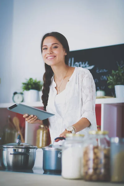 Jovem usando um computador tablet para cozinhar em sua cozinha — Fotografia de Stock