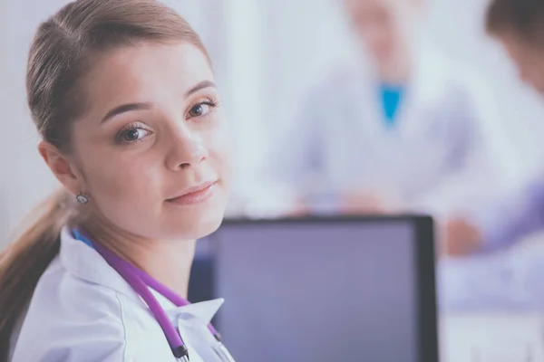 Hermosa joven sonriente doctora sentada en el escritorio — Foto de Stock