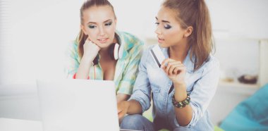 laptop ve kredi sepeti ile evde oturan iki genç kadın