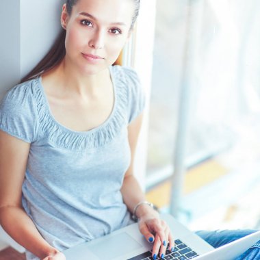 Genç ve güzel bir kadın evde dizüstü bilgisayar kullanıyor.