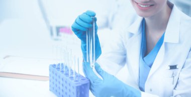 Kadın araştırmacı, beyaz arka planda izole edilmiş ilaç şişeleri ve mataralarla çevrili.