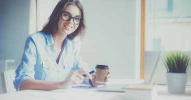 Ofis masasında dizüstü bilgisayarıyla oturan genç bir kadın.