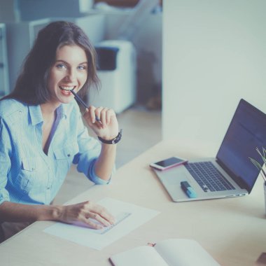 Masasında enstrümanlar, planlar ve dizüstü bilgisayarlarla oturan genç bir kadın.