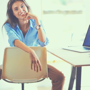 Ofis masasında dizüstü bilgisayarıyla oturan genç bir kadın.