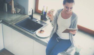 Mutfakta dijital tablet kullanan güzel genç bir kadın.