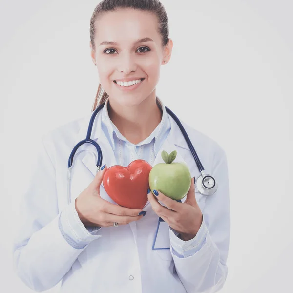 Beautiful smiling female doctor holding red heart and green apple — Stock Photo, Image