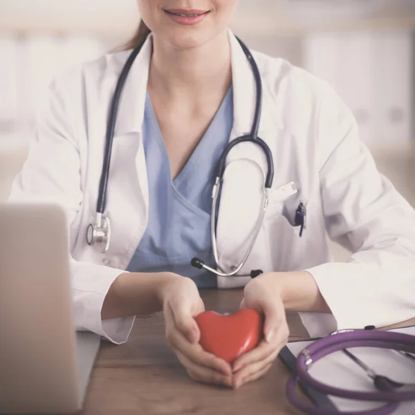 Jonge vrouw arts een rood hart zitten op het Bureau te houden — Stockfoto