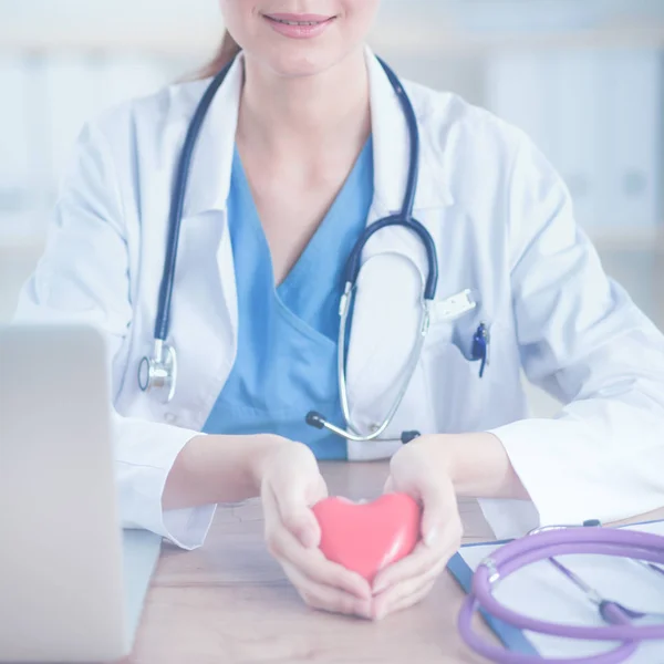 Jeune femme médecin tenant un cœur rouge assis sur le bureau — Photo