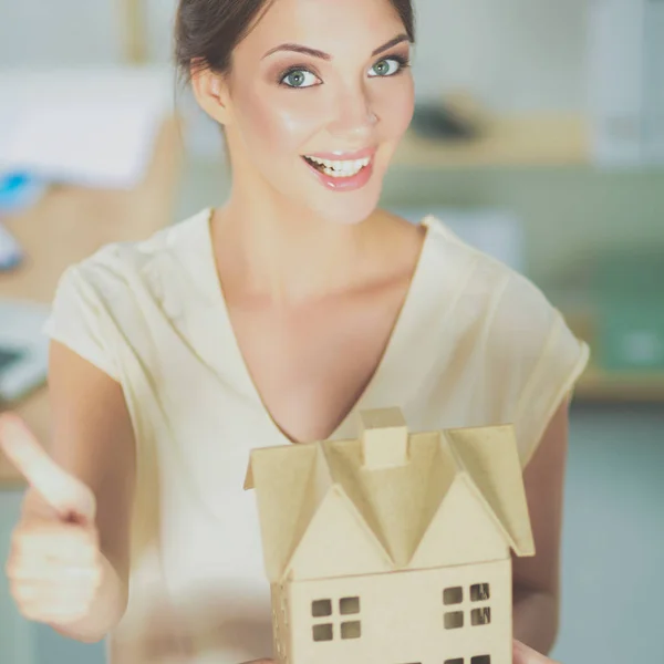 Portrait of female architect holding a little house, standing in office — Stock Photo, Image