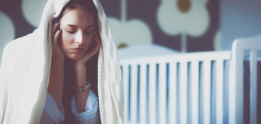 Yatakta çocuk karyolası yakın oturan genç yorgun kadın