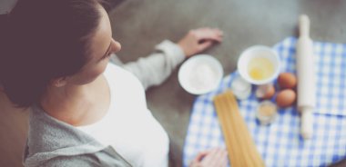 Güzel bir kadın mutfakta pasta pişiriyor. Masanın yanında duruyor.