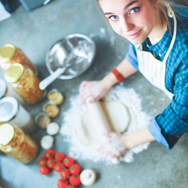 Güzel bir kadın mutfakta pasta pişiriyor. Masanın yanında duruyor.