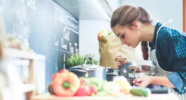 Ung kvinna matlagning i sitt kök står nära spis — Stockfoto