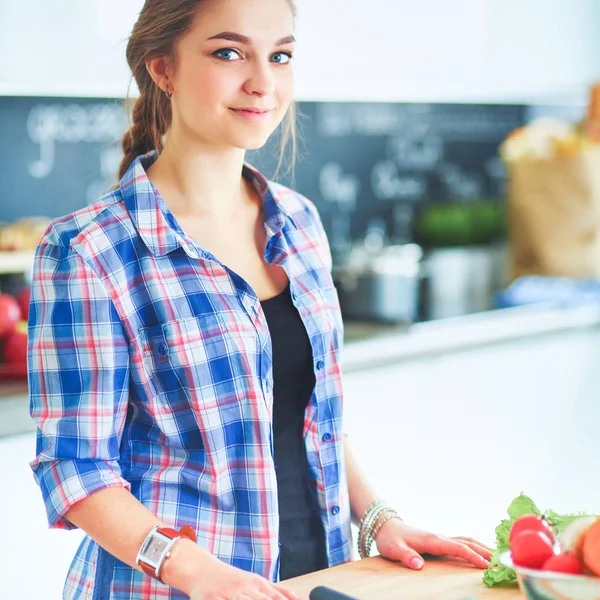 Jonge vrouw snijden van groenten in de keuken in de buurt van bureau — Stockfoto