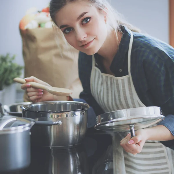 Genç bir kadın mutfağında yemek pişiriyor sobanın yanında duruyor.
