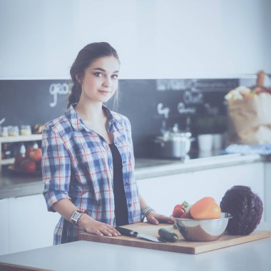 Masanın yanındaki mutfakta sebze doğrayan genç bir kadın.