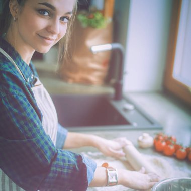 Güzel bir kadın mutfakta pasta pişiriyor. Masanın yanında duruyor.