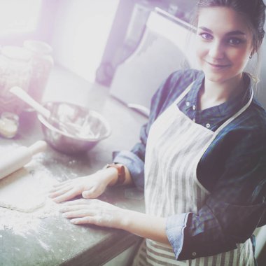 Güzel bir kadın mutfakta pasta pişiriyor. Masanın yanında duruyor.
