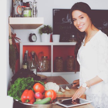 Mutfakta yemek yapmak için tablet bilgisayar kullanan genç bir kadın.