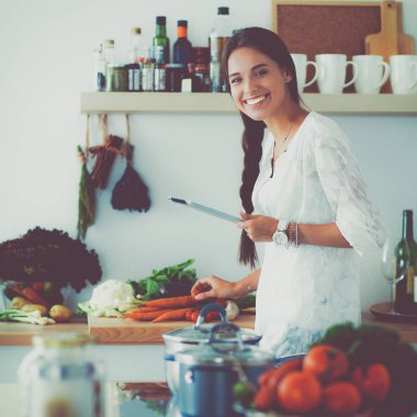 Mutfakta yemek yapmak için tablet bilgisayar kullanan genç bir kadın.