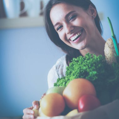 Elinde sebzeli alışveriş torbası tutan genç bir kadın.