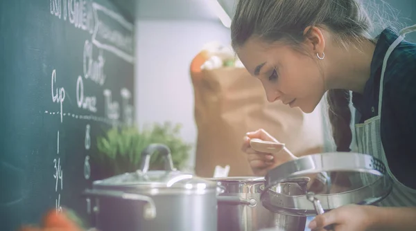 Tânără femeie în picioare de aragaz în bucătărie — Fotografie, imagine de stoc