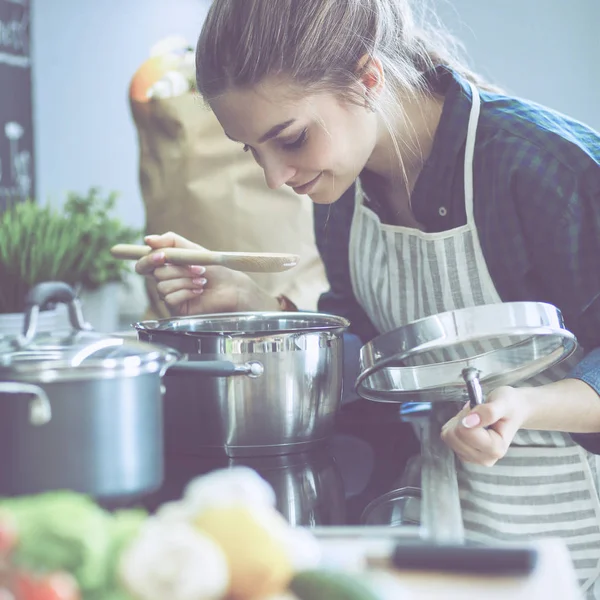 Mujer joven cocinando en su cocina de pie cerca de la estufa — Foto de Stock