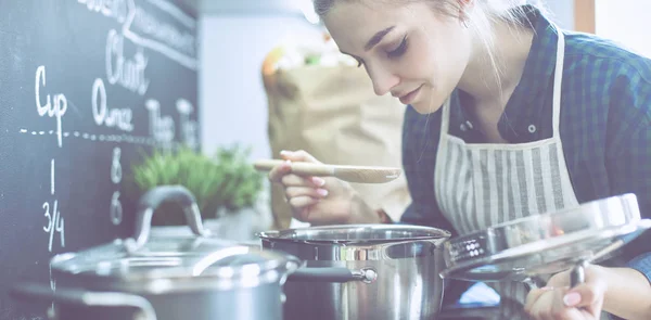 Mujer joven cocinando en su cocina de pie cerca de la estufa — Foto de Stock