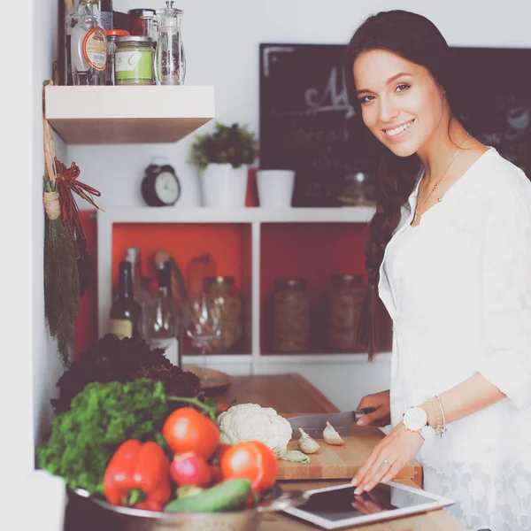 Mutfakta yemek yapmak için tablet bilgisayar kullanan genç bir kadın.