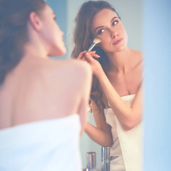 Young woman looking in the mirror and putting make-up on — Stock Photo, Image