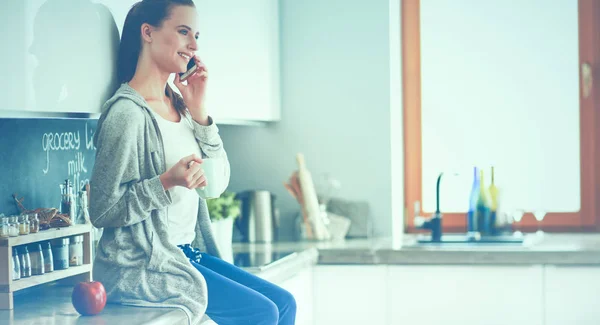 Frau sitzt mit Handy in moderner Küche — Stockfoto