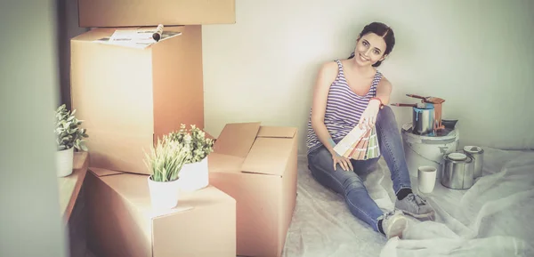 Kvinne som velger maling fra svamp til nytt hjem sittende på tregulv – stockfoto