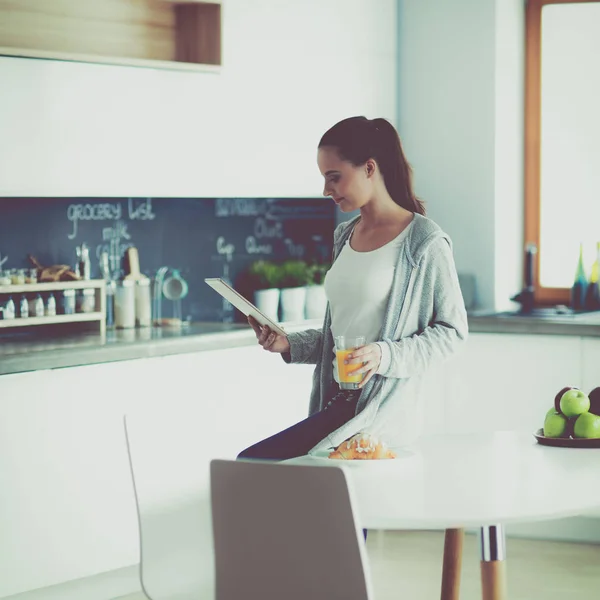 Mujer joven con jugo de naranja y tableta en la cocina —  Fotos de Stock