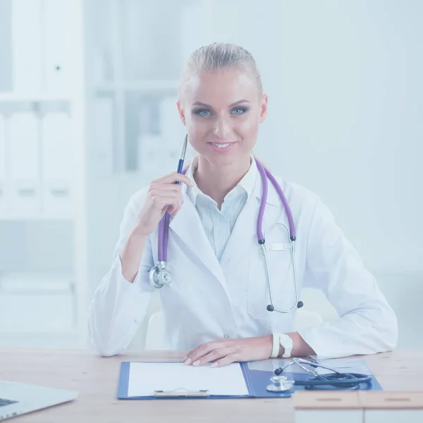 Hermosa joven sonriente doctora sentada en el escritorio y escribiendo. — Foto de Stock