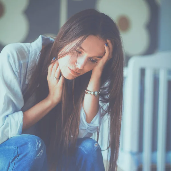 Unga trött kvinna som sitter på sängen nära barnens barnsäng — Stockfoto