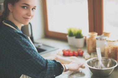 Güzel bir kadın mutfakta pasta pişiriyor. Masanın yanında duruyor.