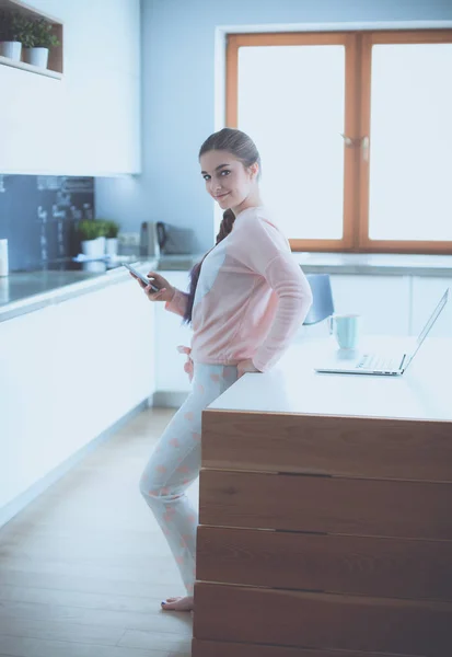 Mujer usando el teléfono móvil de pie en la cocina moderna — Foto de Stock