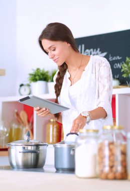 Mutfakta yemek yapmak için tablet bilgisayar kullanan genç bir kadın.