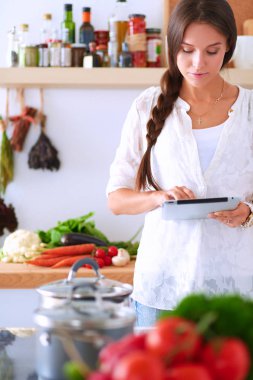 Mutfakta yemek yapmak için tablet bilgisayar kullanan genç bir kadın.
