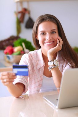 Gülümseyen kadın mutfakta tablet ve kredi kartı kullanarak alışveriş online