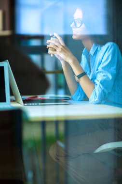 Ofis masasında dizüstü bilgisayarlı genç bir kadın oturuyor, pencereden bakıyor.