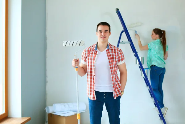 Портрет щаслива усміхнена молода пара малює внутрішню стіну нового будинку — стокове фото