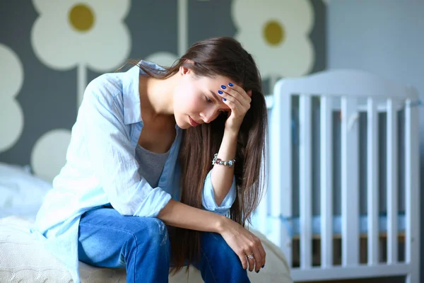 Unga trött kvinna som sitter på sängen nära barnens barnsäng — Stockfoto